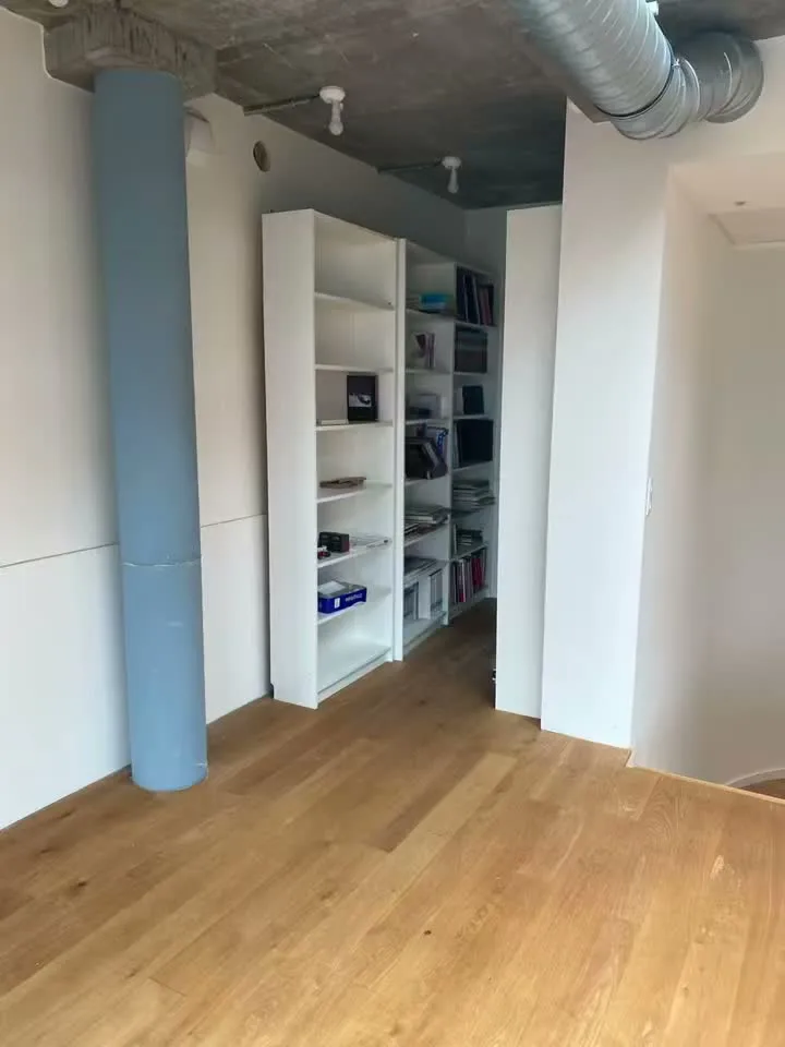 Pièce lumineuse avec parquet et étagères blanches, avant sa transformation en buanderie